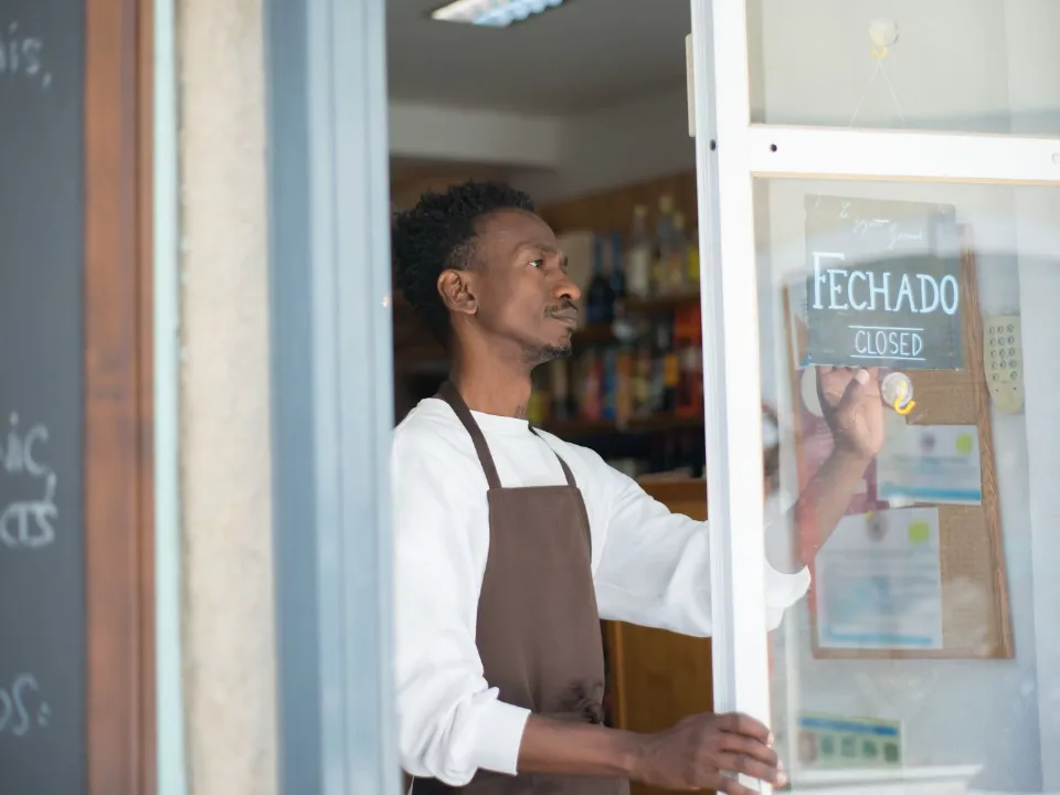 Comerciante na porta da loja, virando a placa de fechado