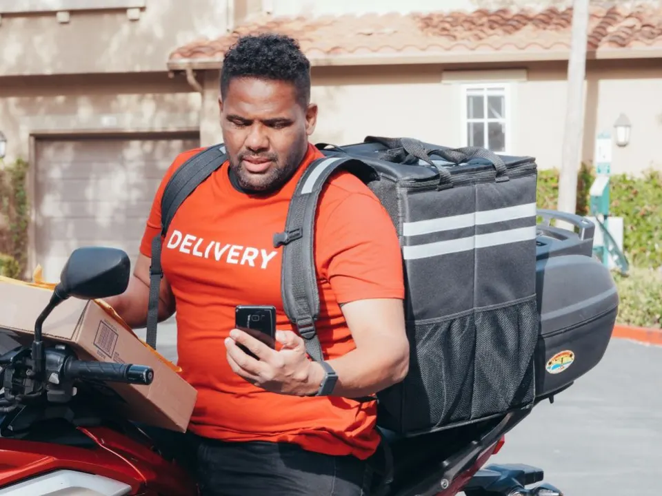 Entregador de aplicativo sentado na moto olhando o celular